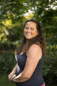 Sonya Dibbin standing in nature surrounded by trees and smiling at the camera